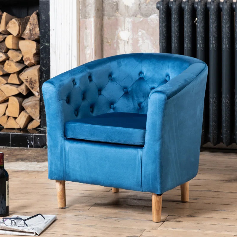 Blue velvet tufted accent armchair with wooden legs in a rustic living room