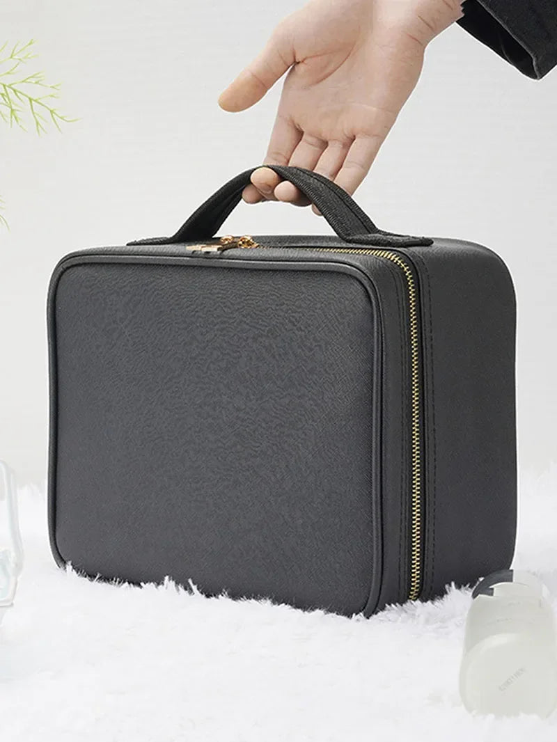 A person holding a black faux-leather travel makeup organizer case with gold zipper details.